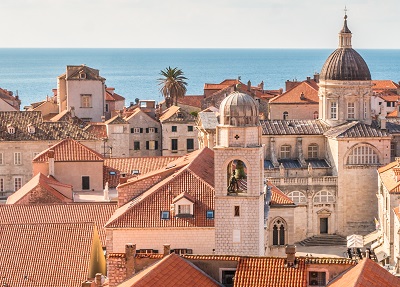 Old buildings in Dubrovnik, Croatia. Orange tile roofs and domed buildings fill the image with the sea in the backgroun.