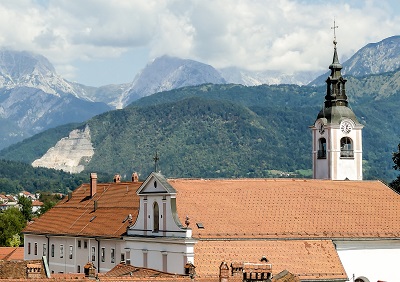 View of old town in Kamink Slovenia. Old church and building roofs in the front, rolling mountains in the back.