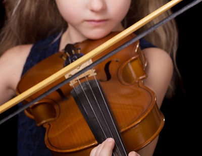 Violin closeup of girl practicing the violin isolated on a black background. Only the bottom half of the girl's face is visible, the focal point is on the violin.