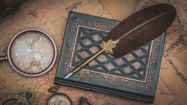 Map of a distant land under a watch, magnifying glass, and book. A pen quill sits on top of the book. 