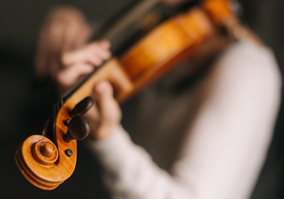 Female musician plays the violin in her home, close-up of the neck of the violin. Her face is not visible.