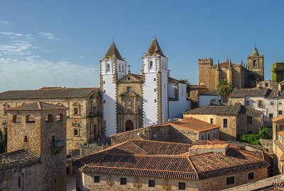 Old town of Caceras, Spain. White towers of a church stand in contracts to brown brick walls and buildings that have orange tile roofs.